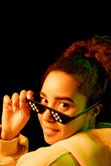 Obraz premium Look back. African-american woman's portrait isolated on dark background in mixed neon light. Wearing trendy pixel eyewear. Concept of human emotions, facial expression, sales, ad, fashion. Copyspace.