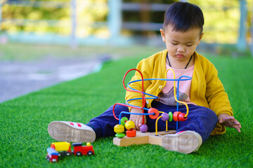 Asian baby boy are playing toys that promote brain and muscular development, A 2-year-old boy in a yellow shirt and blue pants sits on the lawn and casually plays with toys, Child playing.