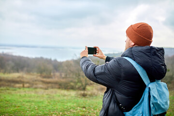 Traveler man with backpack makes photos or selfie on a smartphone