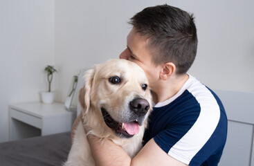Young man hugs a dog at home. A golden retriever happily sits next to a man.