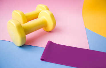 Yellow dumbbell color on pink, blue and yellow mat. Design of a sports poster or banner in fashionable colors of 2021