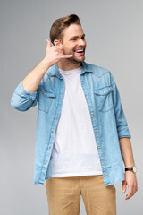 man in jeans shirt making a call me gesture standing over studio grey background