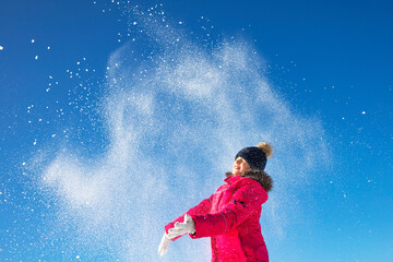 A girl throws snow in the sky. The child plays outside in the winter.