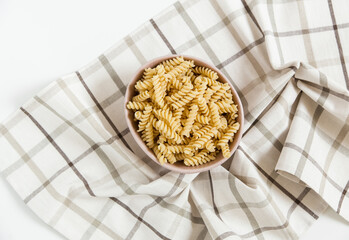uncooked spiral pasta in the ceramic plate. plaid tablecloth background. top view.