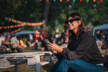 Obraz premium Beautiful female using mobile phone on sunny day on outdoor street fair parade festival
