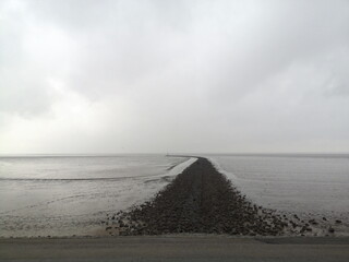 Graue Regenwolken über einer endlosen Mole zum Küstenschutz am Deich an der Küste der Nordsee am...