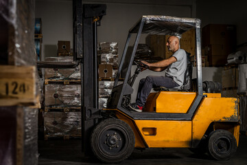 Fototapeta na wymiar Warehouse man worker with forklift. Warehouse worker driver in loading by forklift stack loader