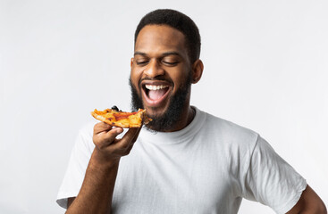 Joyful African Millennial Guy Eating Pizza Slice Over White Background