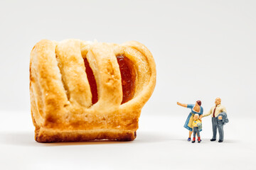 Miniature people. Two adults showing giant pastry to a boy