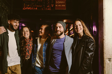 multi ethnic group of young adult friends in front of bar at night smiling