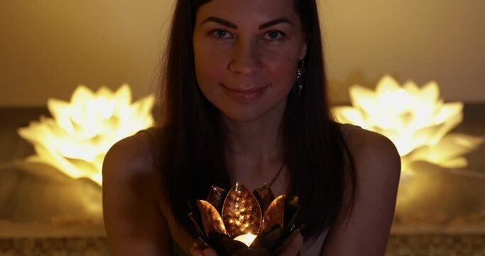 portrait of brunette yogi woman with lotus-shaped candlestick in hands