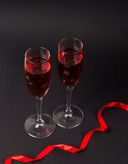 Two Champagne glasses on the black background with a red ribbon. Composition for Valentine's day