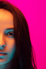 Close up half-full caucasian woman's portrait isolated on pink studio background in mixed neon light. Beautiful female model. Concept of human emotions, facial expression, sales, ad, fashion. Beauty.