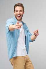 Happy young handsome man in jeans shirt pointing on camera standing against grey background