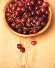 Fresh ripe grape berries in bowl on brown wooden background.