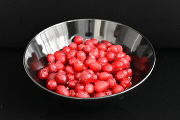 Several berries of natural freshly frozen cranberries in a black ceramic plate, close-up, black background.
