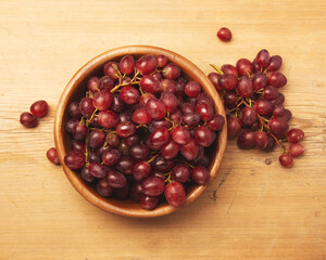 Fresh ripe grape berries in bowl on brown wooden background.