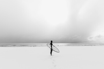 Winter and surfer with surfboard. Snow beach and surfer in wetsuit.