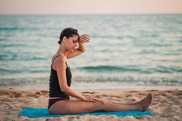 Young beautiful woman practicing pose from yoga on the beach at sunset. Female on beach exercising on vacation