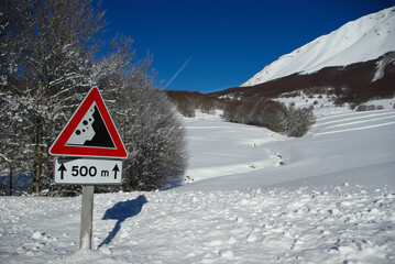 Road sign falling rocks in the snow in the mountains. Indicates danger, it has a triangular shape...
