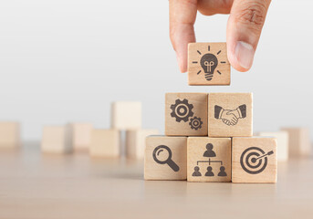 Business strategy, business management or business success concept. Wooden blocks with business icon arranged in pyramid stair shape and a man is holding the top one.