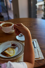 Cropped shot of person drinking tea and eating pancakes at wooden table