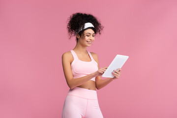 cheerful sportswoman using digital tablet isolated on pink