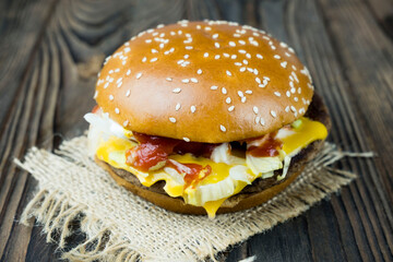Close-up of a delicious fresh homemade burger with lettuce, cheese, onions and tomatoes on a wooden table, the concept of a mouth-watering meal