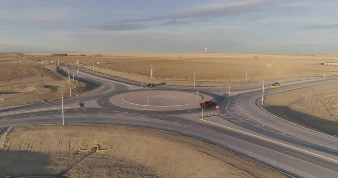Cars and pickup trucks navigate a modern roundabout in the middle of the countryside.