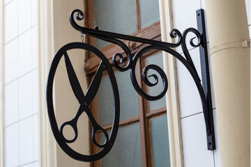 An old barbershop sign on the front of the building, Black scissors in an oval on a foreigned stand.
