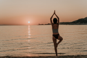 Fototapeta na wymiar Young beautiful woman practicing pose from yoga on the beach at sunset. Female on beach exercising on vacation