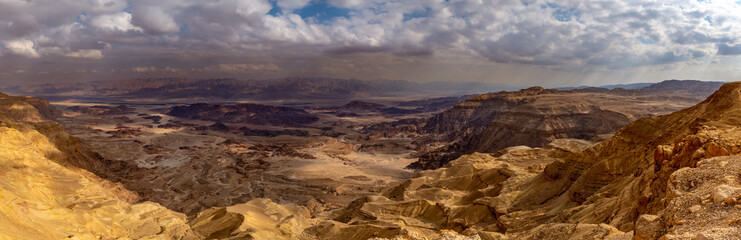 Fototapeta na wymiar A desert canyon scene with dramatic drop and mountains and heavy cloudy sky. Timna Crater, Israel