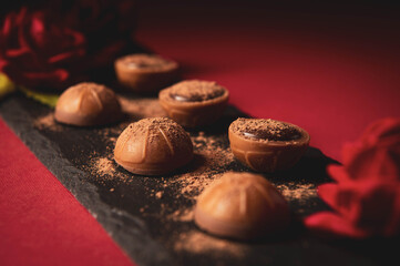 Chocolates lie on a slate on a red table surface. Festive table setting. Dessert serving. Romance. A romantic dessert for the holiday. Sweet gift.