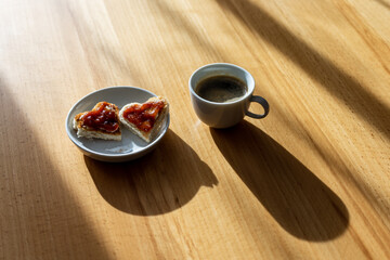 Zwei Toastscheiben in Herzform mit Konfitüre auf enem Teller und eine Tasse Kaffee auf einem Holz Tisch. Schlagschatten, Frühstück, Muttertag.