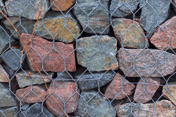 Fragment of a gabion close-up, stones and minerals of different colors, sizes and shapes in a metal mesh