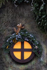A fragment of the decor of a New Year's house, a round window decorated with fir branches and cones, along which a squirrel and its cub climb, New Year and Christmas card