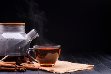 A hot teacup with herbs was placed on an old wooden table in a black background, a gentle sunlight shone in a warm atmosphere.