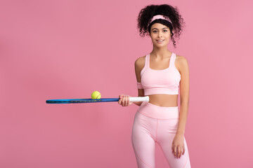 happy and sportive woman holding tennis racket with ball isolated on pink