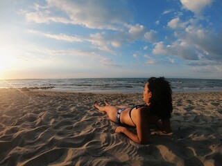 Mujer morena acostada en la playa viendo el atardecer
