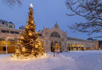 A beautifully decorated Christmas tree glowing in front of the historic colonnade in a snowy winter evening. A festive holiday atmosphere in a famous spa town