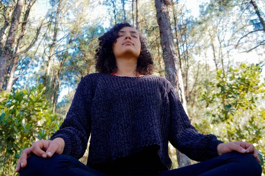 Mujer en postrura de meditacion en el bosque usando ropa negra
