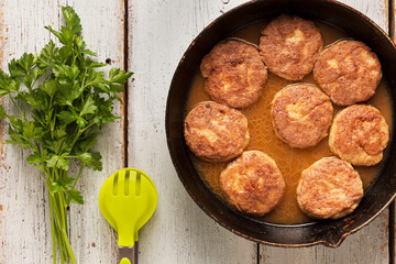 Meat cutlets on a vintage frying pan close-up on a wooden table, top view