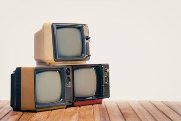 Pile of three old vintage TVs on wooden table on white background