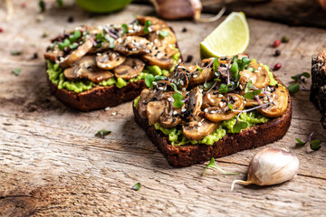Fototapeta na wymiar Avocado sandwiches with fried mushrooms, sesame on a wooden background. Bruschetta. Vegetarian food. Clean eating. Top view. Copy space