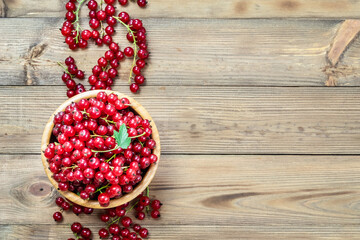 Red currant in a bowl on wooden background. Top view, copy space.
