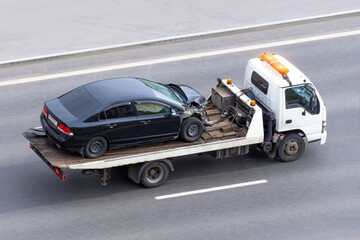 Wrecked car after an accident on a tow truck transported on a highway.