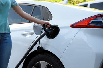 Woman inserting plug into electric car socket at charging station, closeup