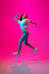 Fototapeta na wymiar Jumping high, looks cheerful. Caucasian woman's portrait on pink studio background in mixed neon light. Stylish outfit. Concept of human emotions, facial expression, sales, ad, fashion. Copyspace.