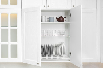 Open cabinet with different clean dishware in kitchen - obrazy, fototapety, plakaty