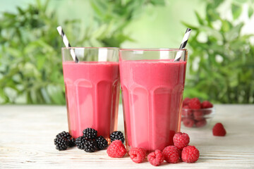 Tasty fresh milk shakes with berries on white wooden table against blurred background